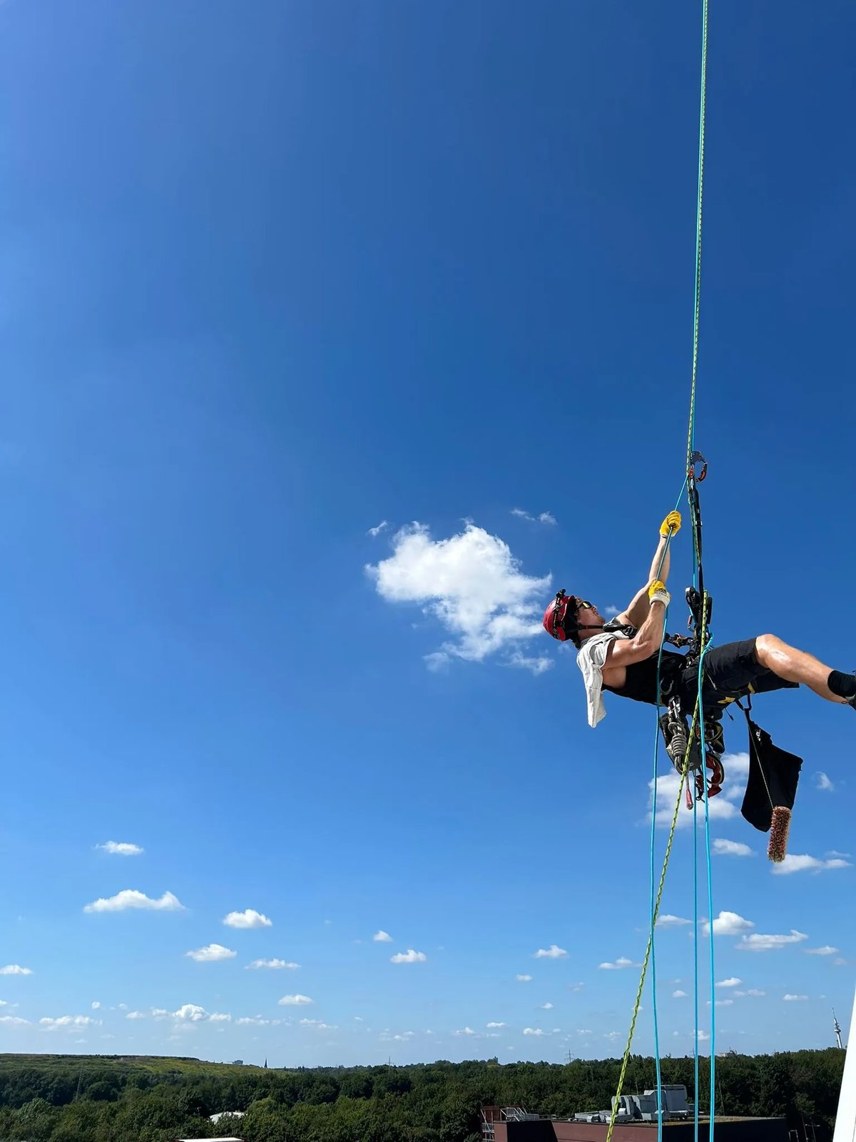 Industriekletterer beim Abseilen mit Reinigungsbürste vor blauem Himmel im Seilzugang