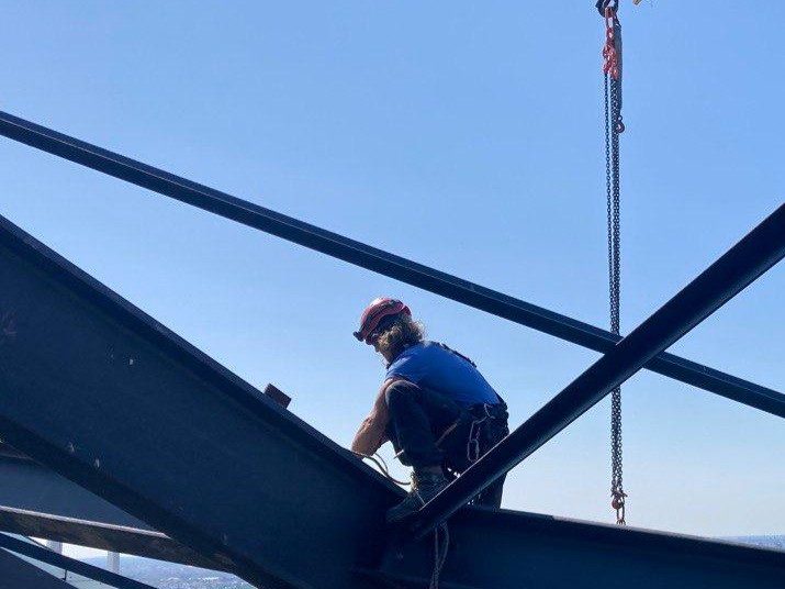 Seilzugangstechniker montiert Stahlbauteile in großer Höhe mit Kranunterstützung